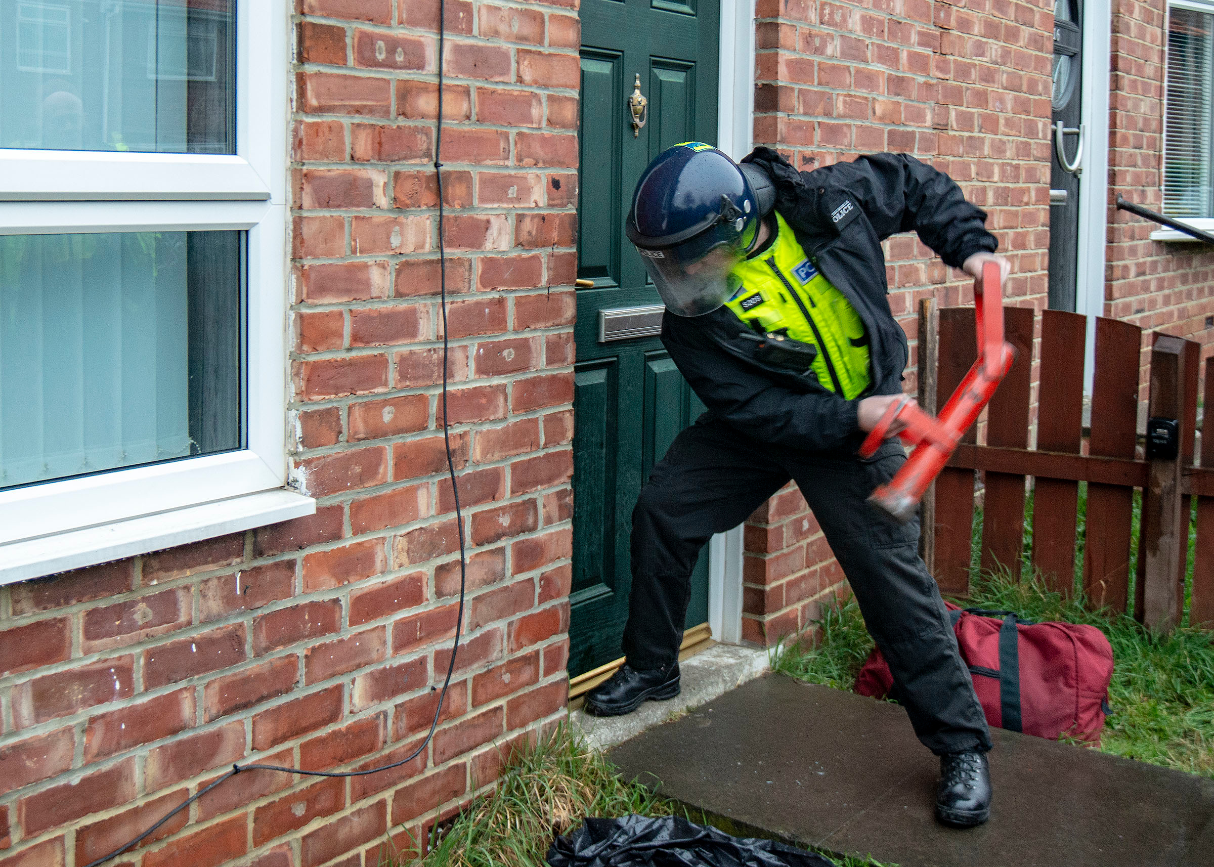 Police officer putting a door in with a large heavy red tool